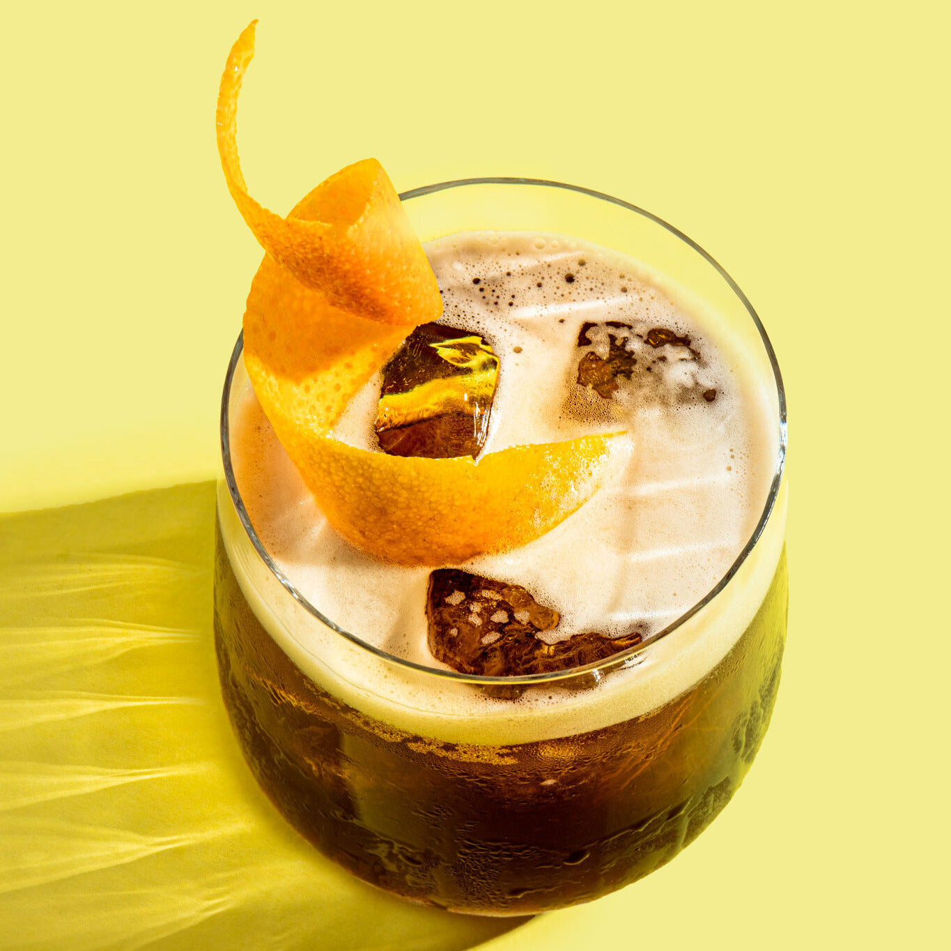 Erfrischender alkoholfreier Espresso Sour in einem Tumblerglas mit Eis und Orangenzeste, daneben POLLY Espresso Aperitif.