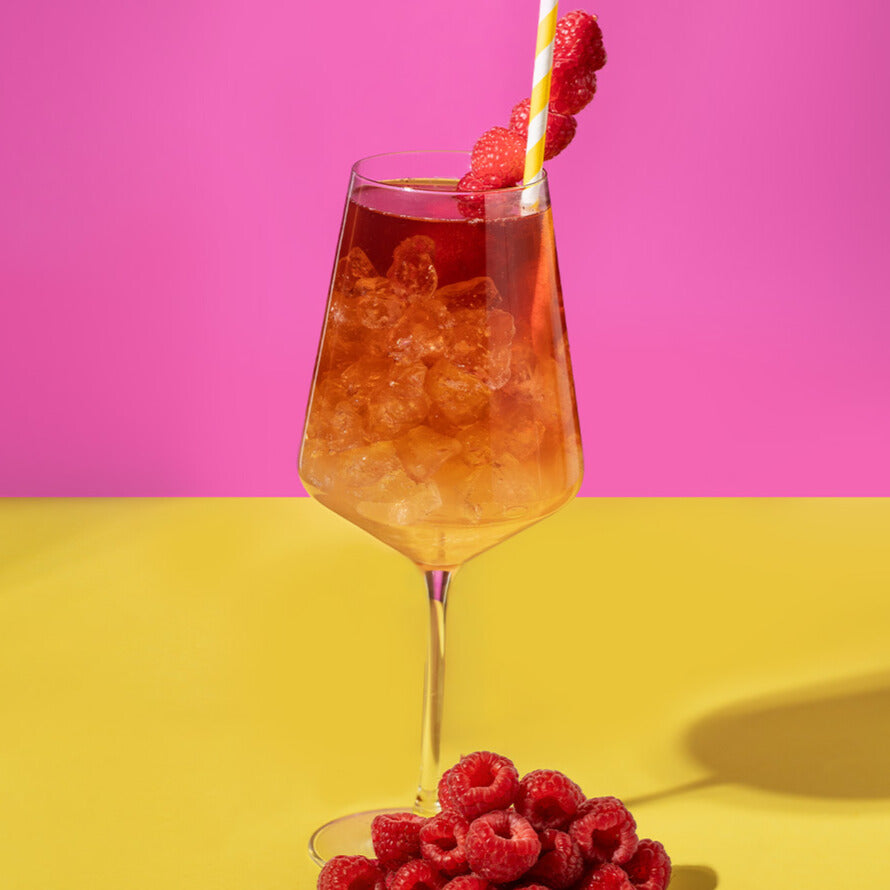 Ein Glas Himbeer-Yuzu-Spritz mit POLLY Citrus Aperitif und Bionade Himbeer-Pflaume, garniert mit Himbeeren.