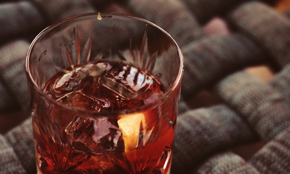 Gin/POLLY and Juice mit Zitronenzeste im Glas auf einem Flechttisch