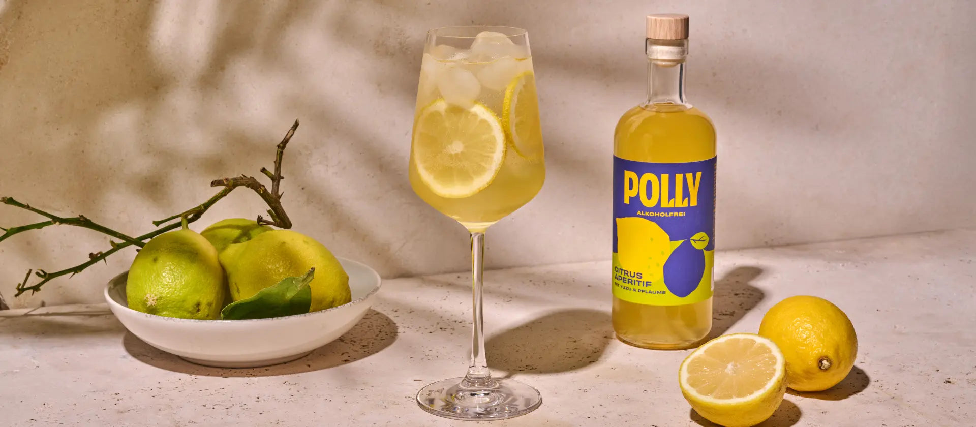 Glas mit alkoholfreiem Citrus Spritz Getränk neben einer POLLY Flasche Citrus Aperitif