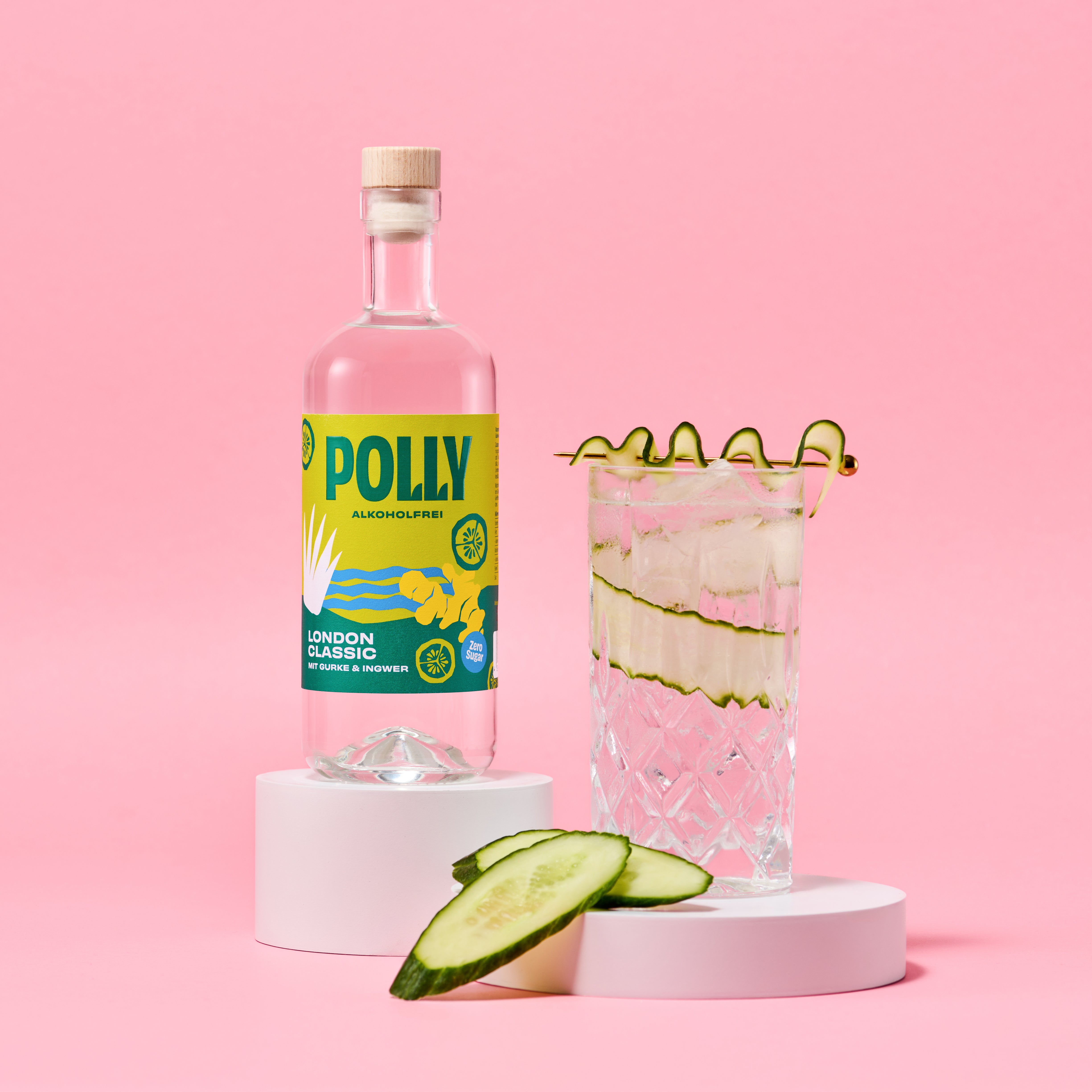 Eine Flasche POLLY London Classic der Polly GmbH steht neben einem hohen Glas Gurke Ingwer Getränk mit Gurkenbändern vor einem rosa Hintergrund und Gurkenscheiben davor.